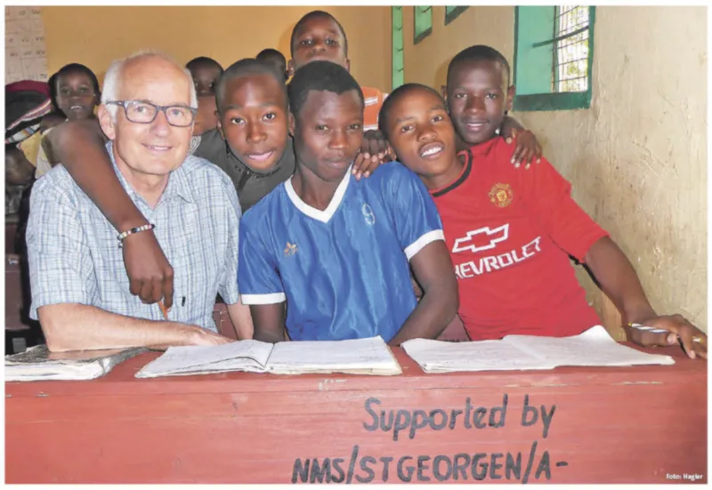 Markus Hagler mit Schülern in Tansania an einer Schulbank mit der Aufschrift „Supported by NMS St. Georgen/A.“